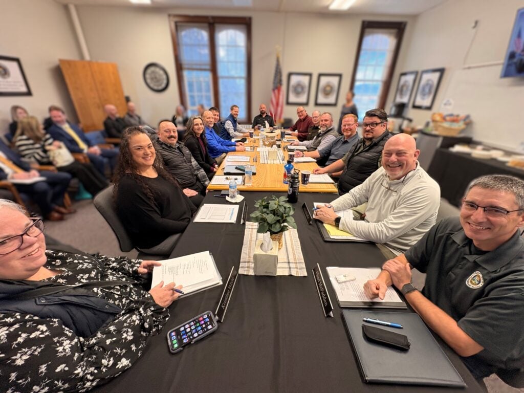 Photograph of the Montana POST Council's February 25, 2026, meeting. Council members and staff sitting around a table. Clockwise from bottom left: Kristine White, Chanel Waples, Brian Casey, Shellie Brady, Bill Smith, General Counsel Stuart Segrest, Jesse Slaughter, Jim Thomas, Leo Dutton, Mark Craft, Jim Anderson, Anthony Hutchings, John Shaffer, and POST Investigator Chad McFadden.